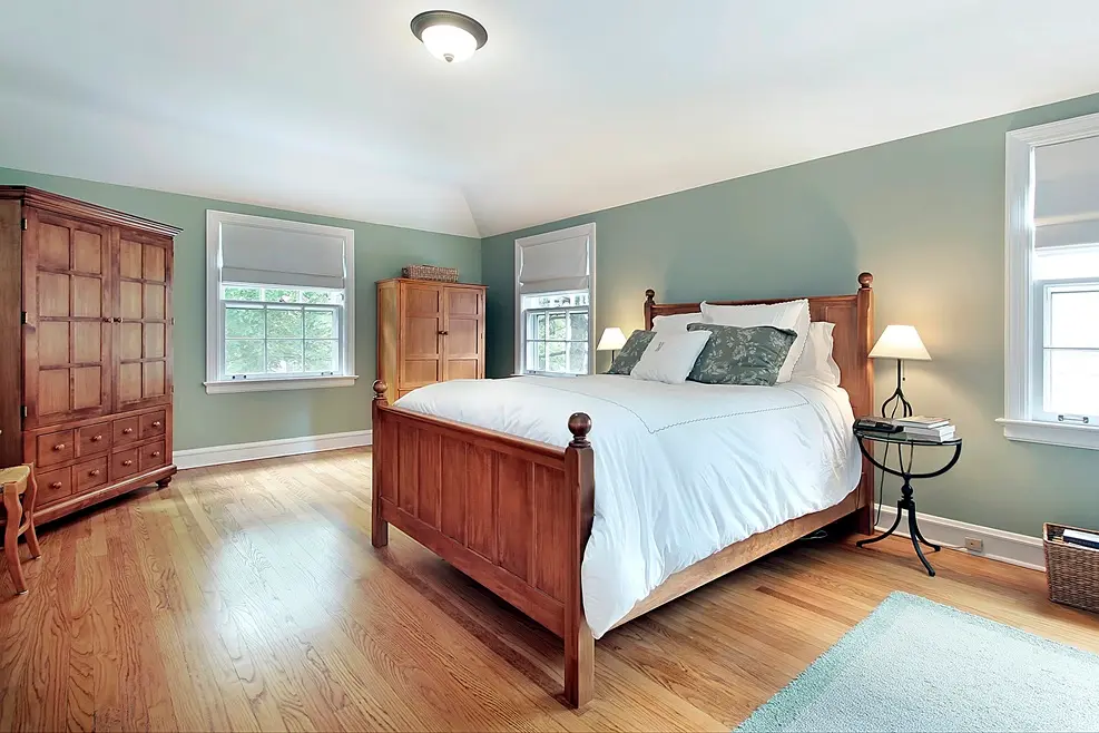 Accessible aging-in-place master bedroom with wood furniture and calming green walls, designed for comfort and ease of mobility.
