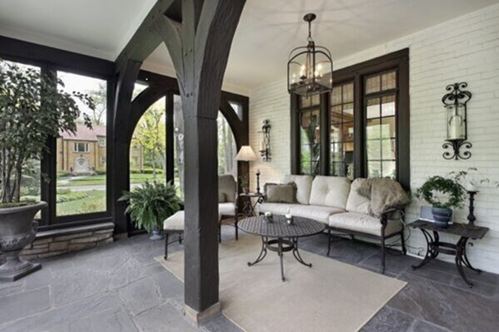 Covered porch with wood beams, stone flooring, and outdoor furniture overlooking a landscaped yard.